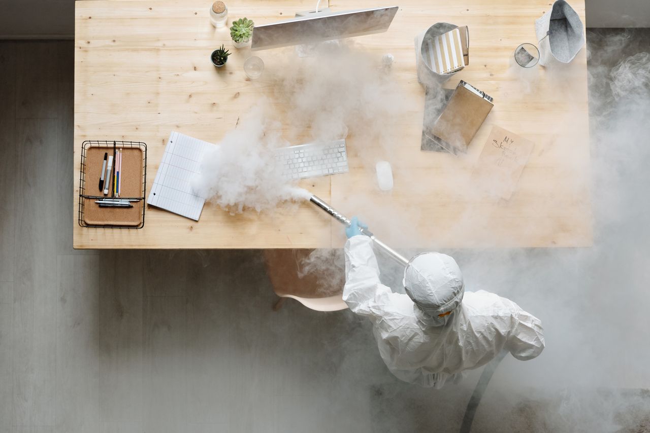 services-04 An individual disinfects a workspace using fumigation, wearing full protective gear for safety.